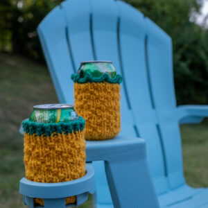 Two knitted cozies to resemble pineapples sitting on a blue adirondack chair