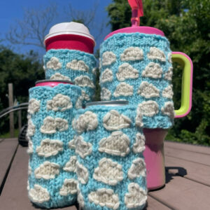 Four knitted drink cozies featuring a light blue background with knitted cloud details in a repeating pattern. Cozies include coffee sleeve, soda pop can cozy, tall skinny energy drink cozy, 40 oz tumbler sweater cozy
